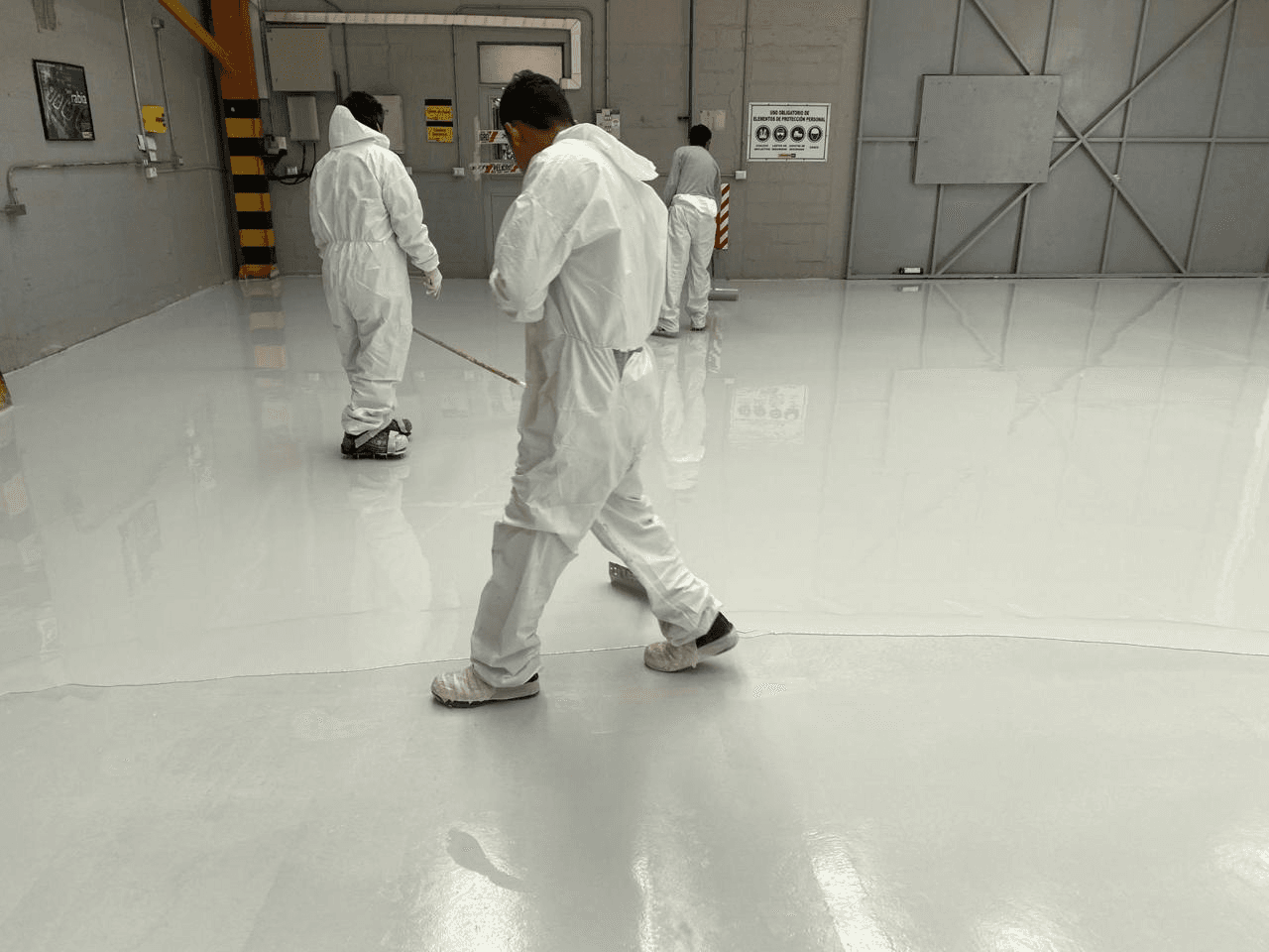 Equipo de trabajadores en trajes de protección aplicando piso epóxico
